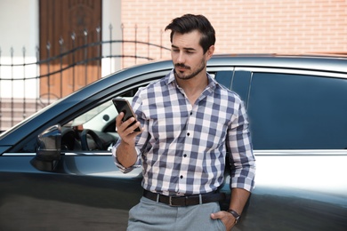 Photo of Attractive young man with smartphone near luxury car outdoors