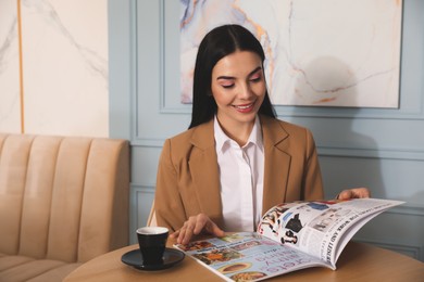 Photo of Woman with cup of coffee reading magazine at cafe in morning