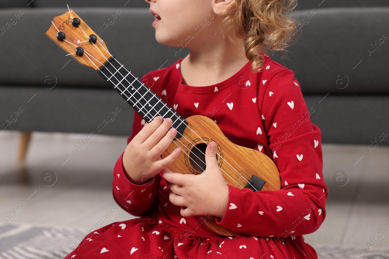 Photo of Little girl playing toy guitar at home, closeup