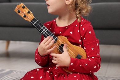 Photo of Little girl playing toy guitar at home, closeup