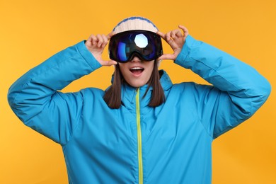 Winter sports. Surprised woman with snowboard goggles on orange background