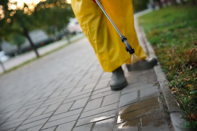 Photo of Person in hazmat suit disinfecting street pavement with sprayer, closeup. Surface treatment during coronavirus pandemic