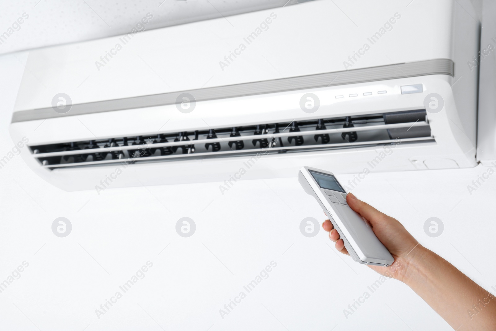 Photo of Woman operating air conditioner with remote control indoors, closeup