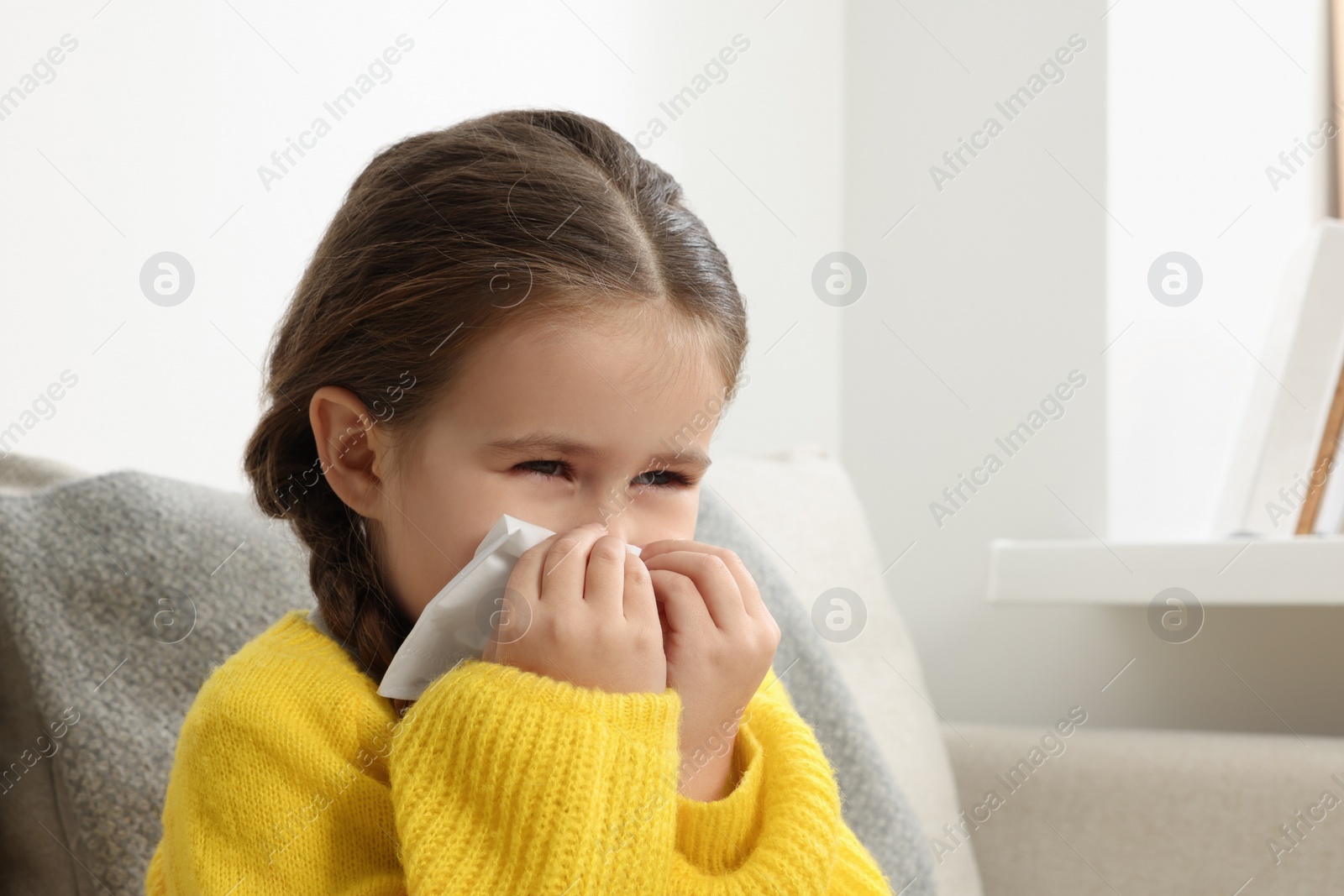 Photo of Girl blowing nose in tissue on sofa in room. Cold symptoms