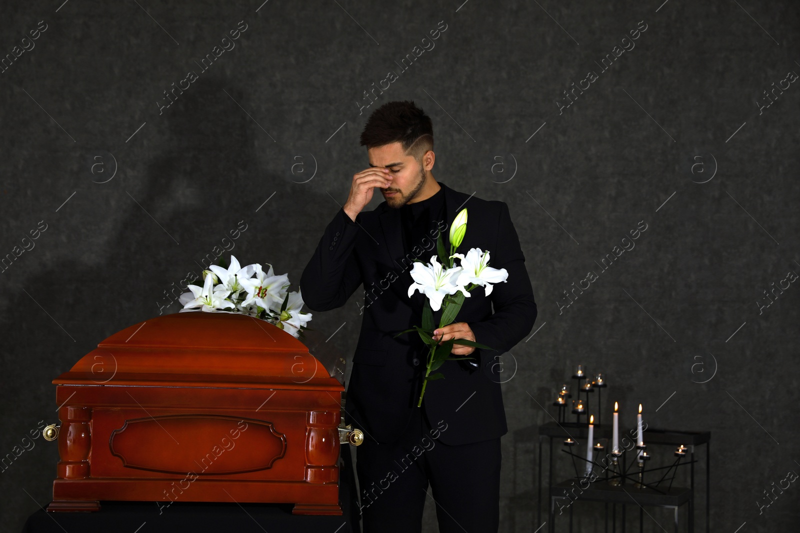 Photo of Sad young man with white lilies near casket in funeral home