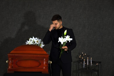 Photo of Sad young man with white lilies near casket in funeral home