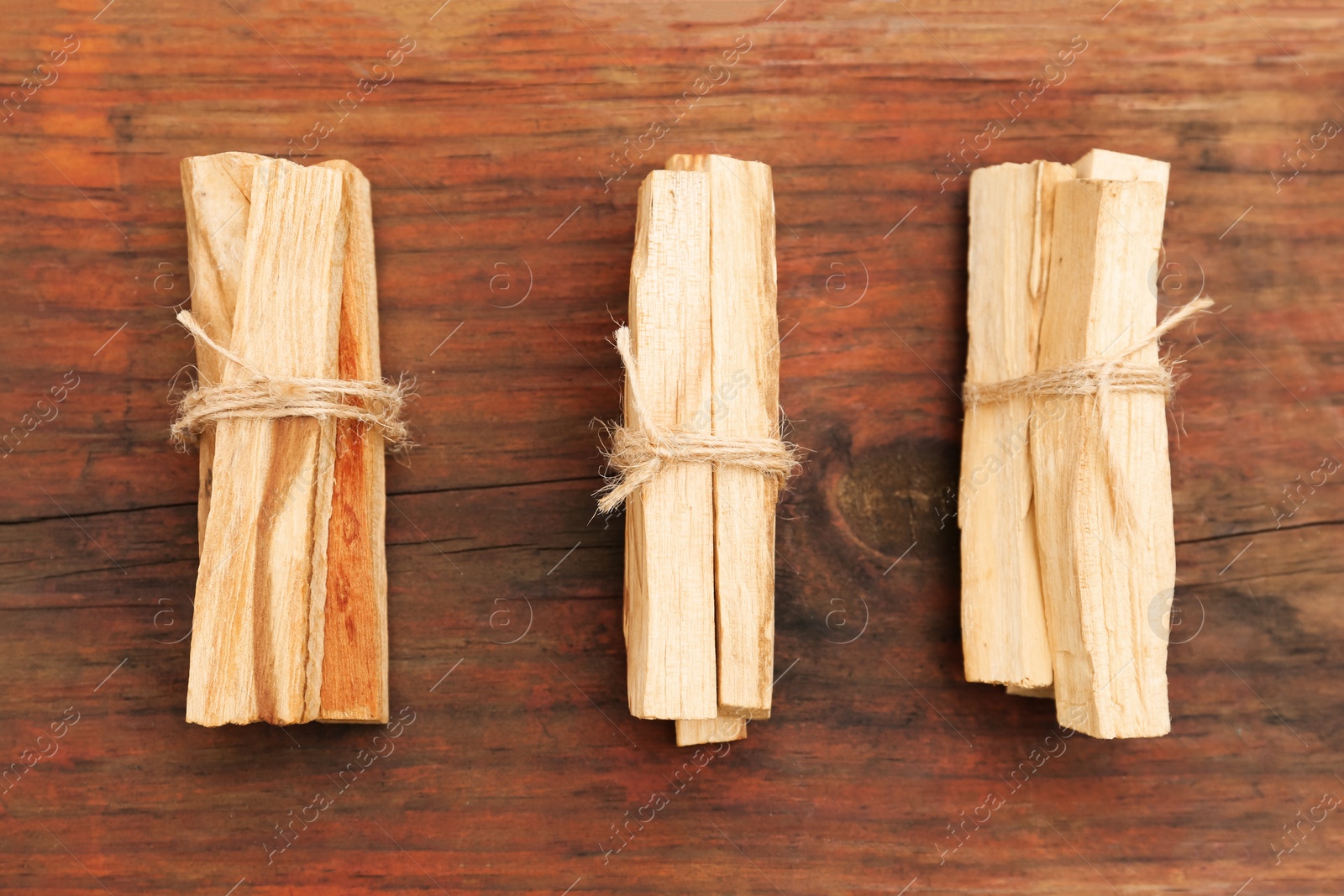 Photo of Bunches of tied Palo Santo sticks on wooden table, flat lay