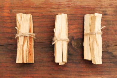 Photo of Bunches of tied Palo Santo sticks on wooden table, flat lay