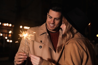 Couple in warm clothes holding burning sparklers at night
