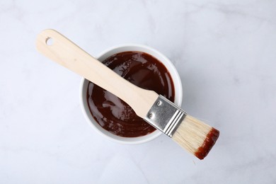 Marinade in bowl and basting brush on white marble table, top view