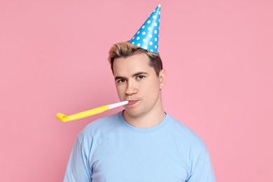 Photo of Sad young man with party hat and blower on pink background