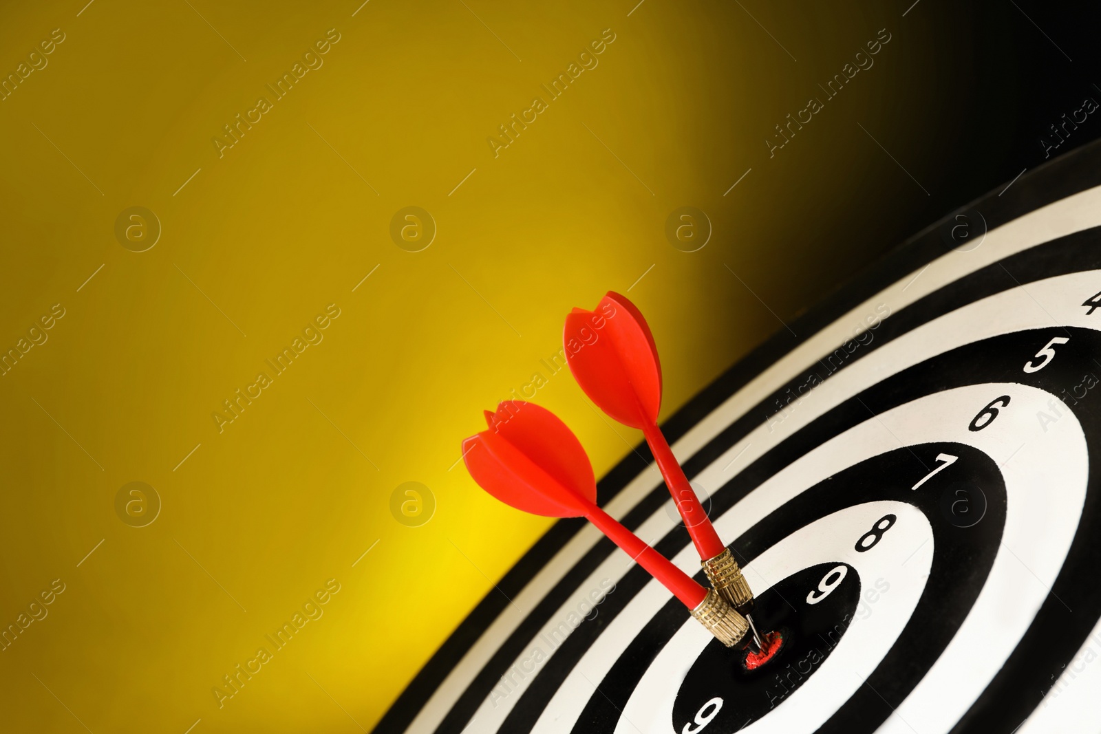 Photo of Red arrows hitting target on dart board against yellow background. Space for text