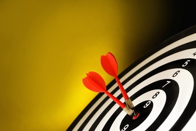 Photo of Red arrows hitting target on dart board against yellow background. Space for text