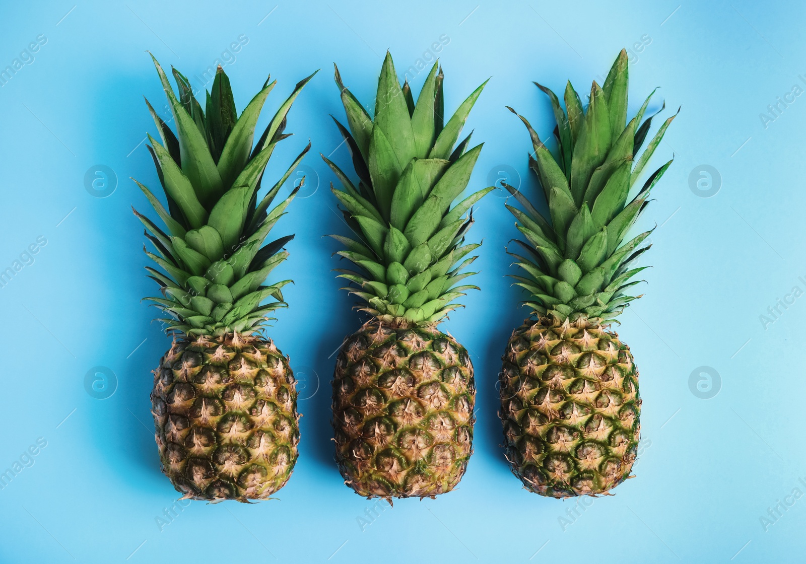 Photo of Fresh ripe juicy pineapples on light blue background, flat lay