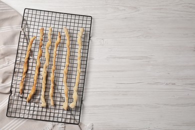 Photo of Rack with homemade breadsticks on white wooden table, top view and space for text. Cooking traditional grissini