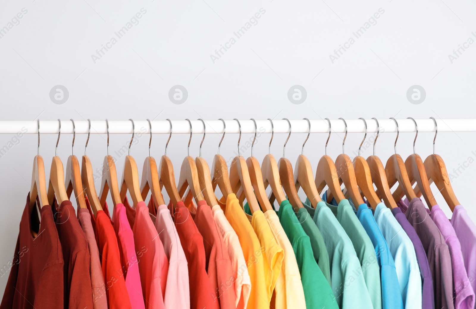 Photo of Rack with rainbow clothes on light background