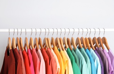 Photo of Rack with rainbow clothes on light background