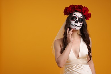 Photo of Young woman in scary bride costume with sugar skull makeup and flower crown on orange background, space for text. Halloween celebration