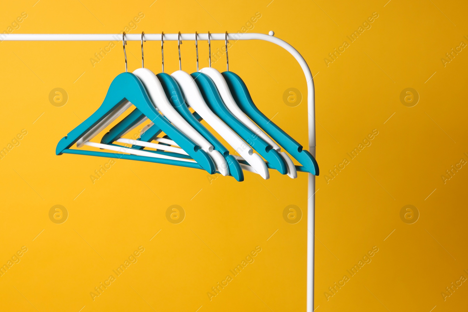 Photo of Bright clothes hangers on metal rack against yellow background