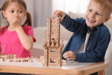 Photo of Little girl and boy playing with wooden tower at table indoors, selective focus. Children's toy