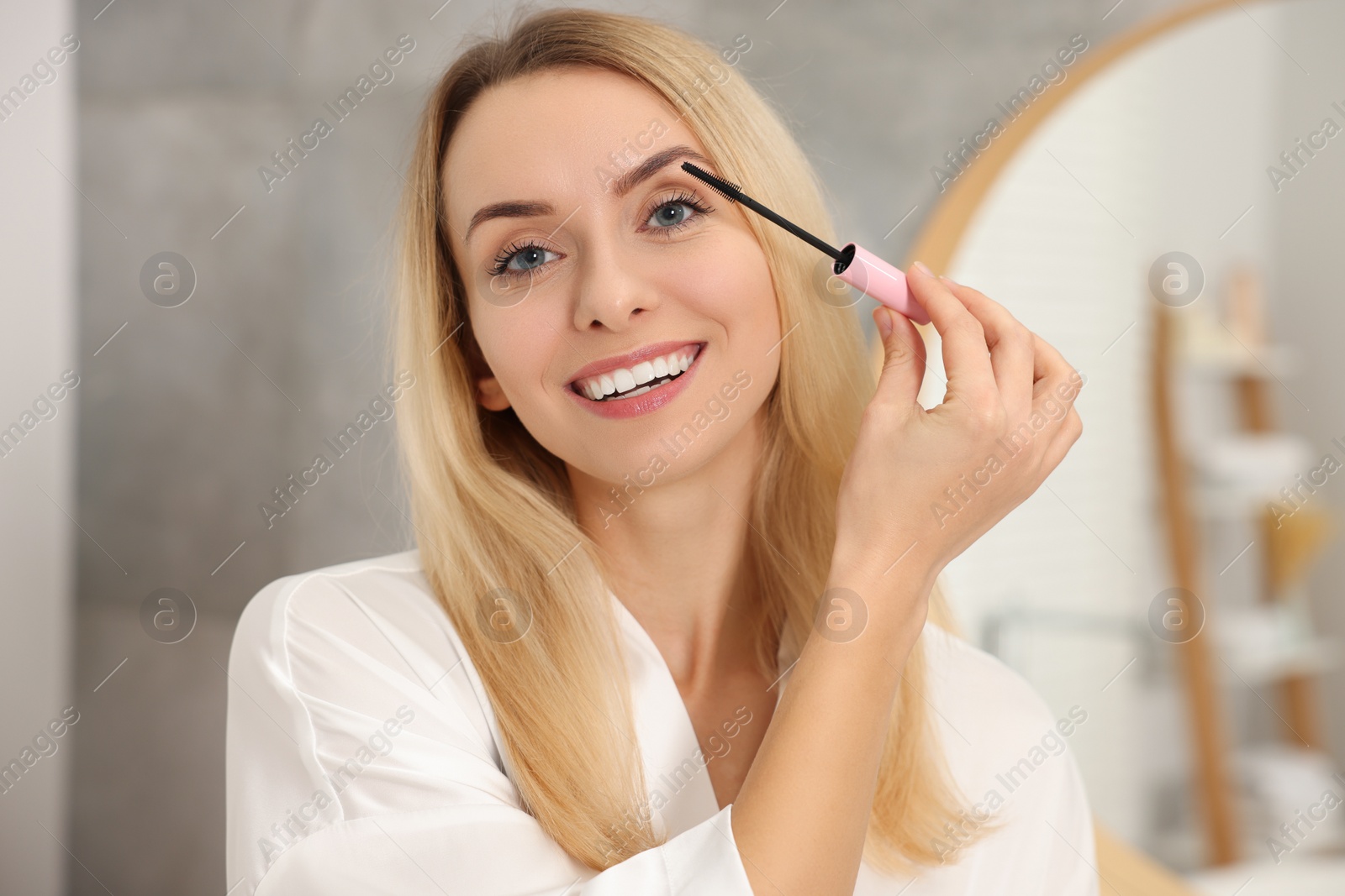 Photo of Beautiful woman applying mascara with brush indoors