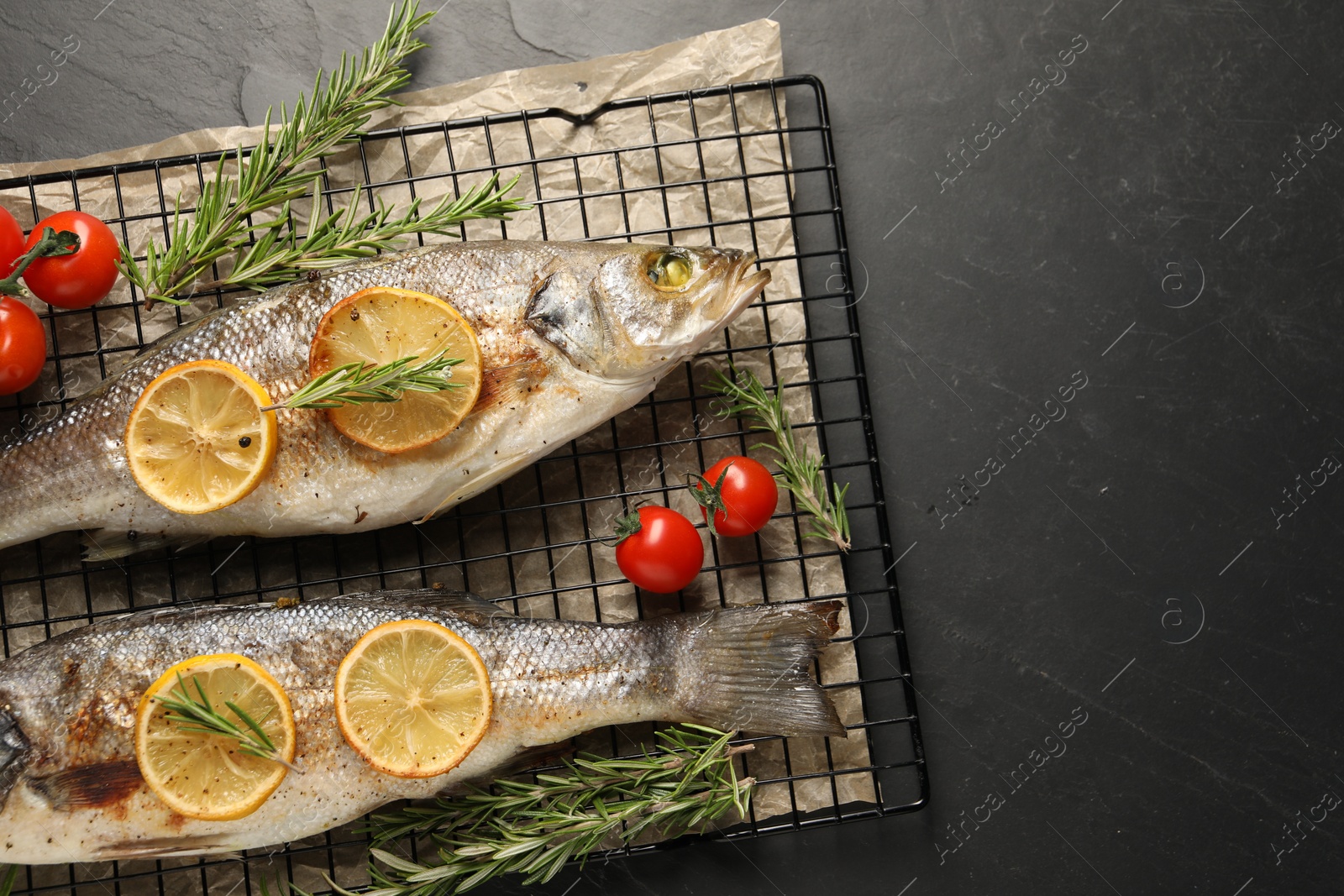 Photo of Baked fish with tomatoes, rosemary and lemon on black textured table, top view. Space for text