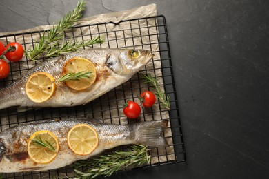 Photo of Baked fish with tomatoes, rosemary and lemon on black textured table, top view. Space for text