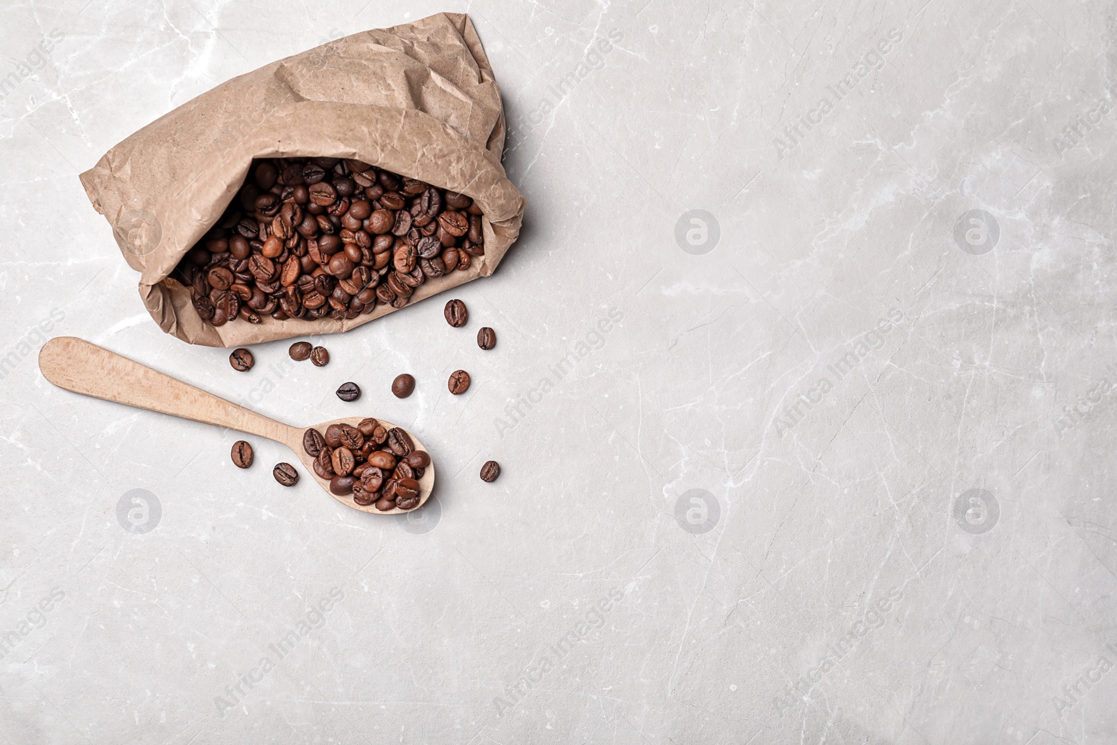 Photo of Spoon and paper bag with coffee beans on light background, top view