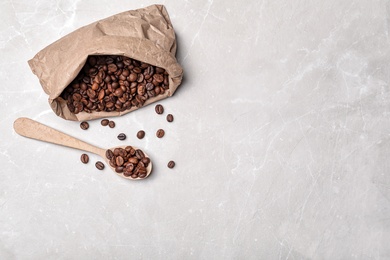 Spoon and paper bag with coffee beans on light background, top view