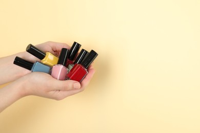 Photo of Woman holding nail polishes on beige background, closeup. Space for text