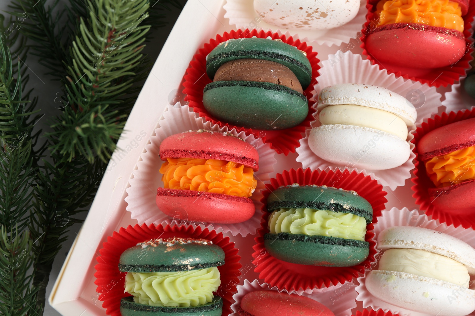 Photo of Different tasty Christmas macarons in box and fir branches on table, flat lay