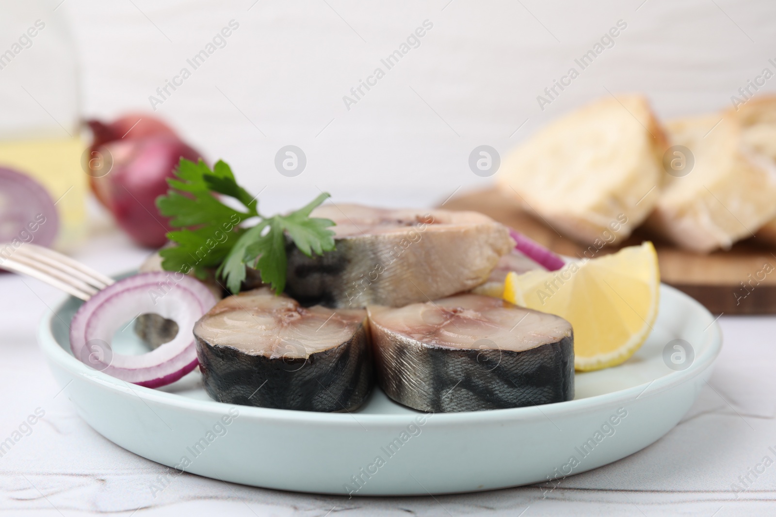 Photo of Slices of tasty salted mackerel with parsley, onion ring and lemon wedge on light table, closeup