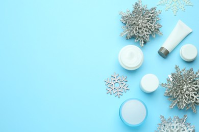 Photo of Flat lay composition with cosmetic products and snowflakes on light blue background, space for text. Winter skin care