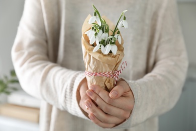 Photo of Woman holding paper bag with beautiful snowdrops and traditional cord martisor indoors, closeup. Symbol of first spring day