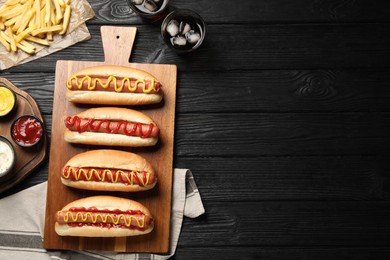 Photo of Delicious hot dogs with mustard, ketchup and potato fries on black wooden table, flat lay. Space for text