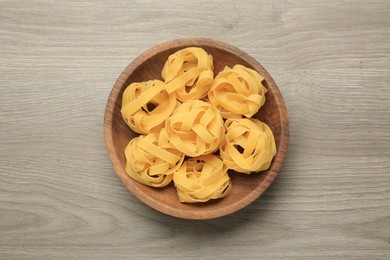Photo of Raw tagliatelle pasta in bowl on light grey wooden table, top view