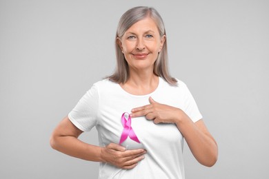 Photo of Beautiful senior woman with pink ribbon on light grey background. Breast cancer awareness