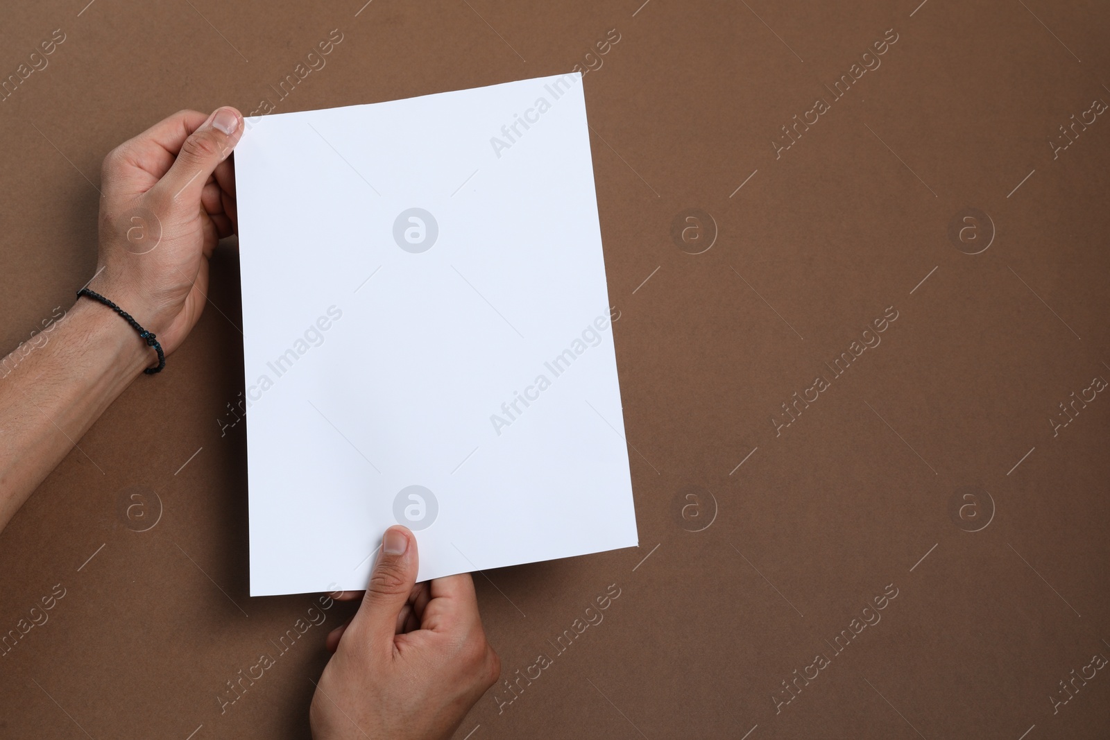 Photo of Man holding sheet of paper on brown background, closeup. Mockup for design