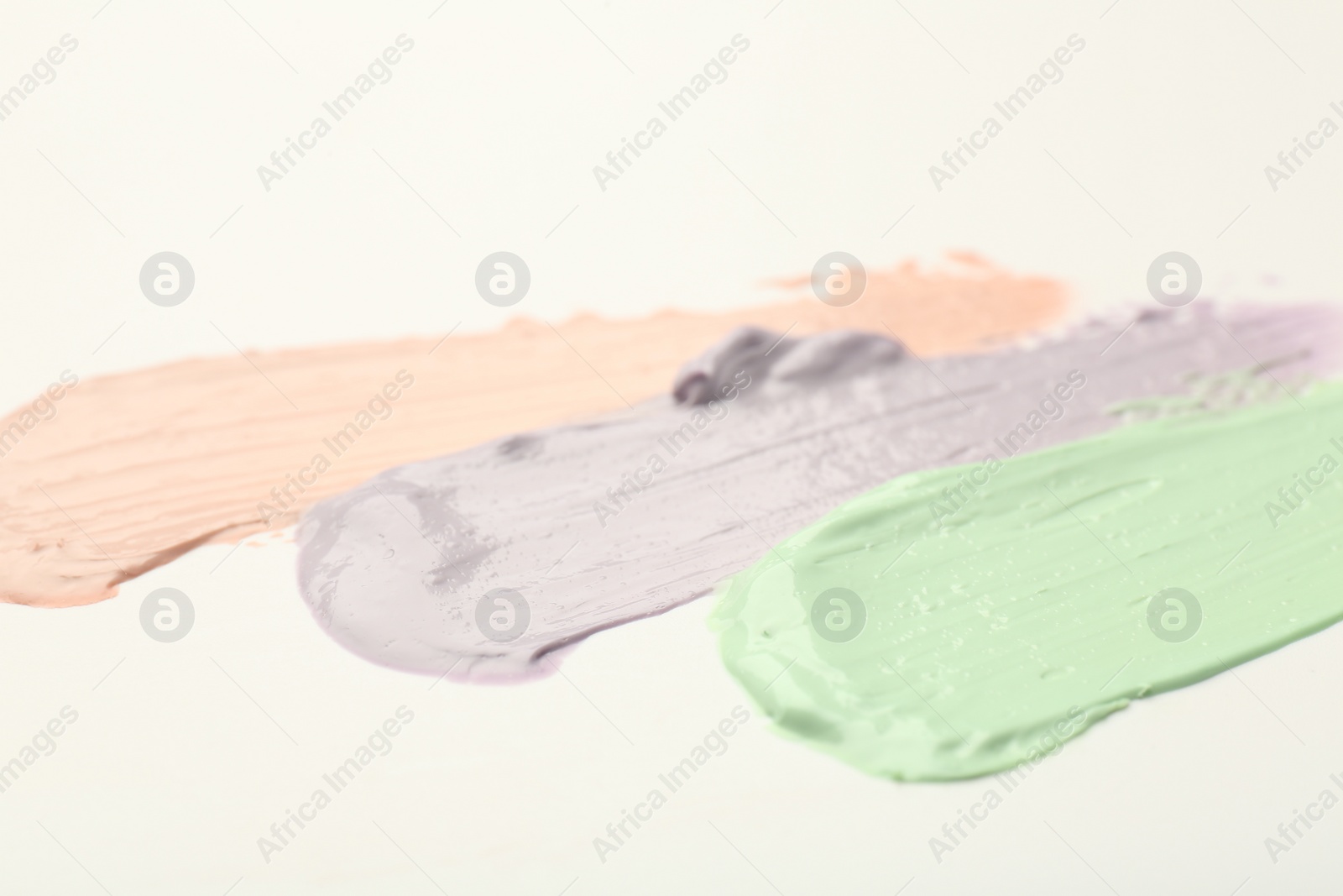 Photo of Strokes of pink, green and purple color correcting concealers on white background, closeup