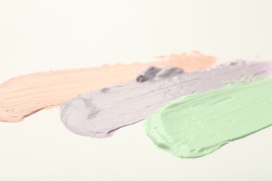 Strokes of pink, green and purple color correcting concealers on white background, closeup