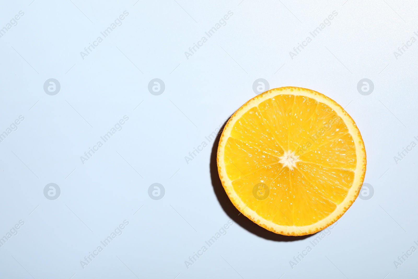 Photo of Slice of juicy orange on light blue background, top view. Space for text