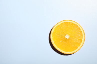 Slice of juicy orange on light blue background, top view. Space for text