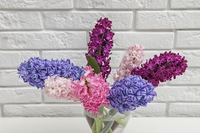 Photo of Beautiful hyacinths in glass vase on table against brick wall. Spring flowers