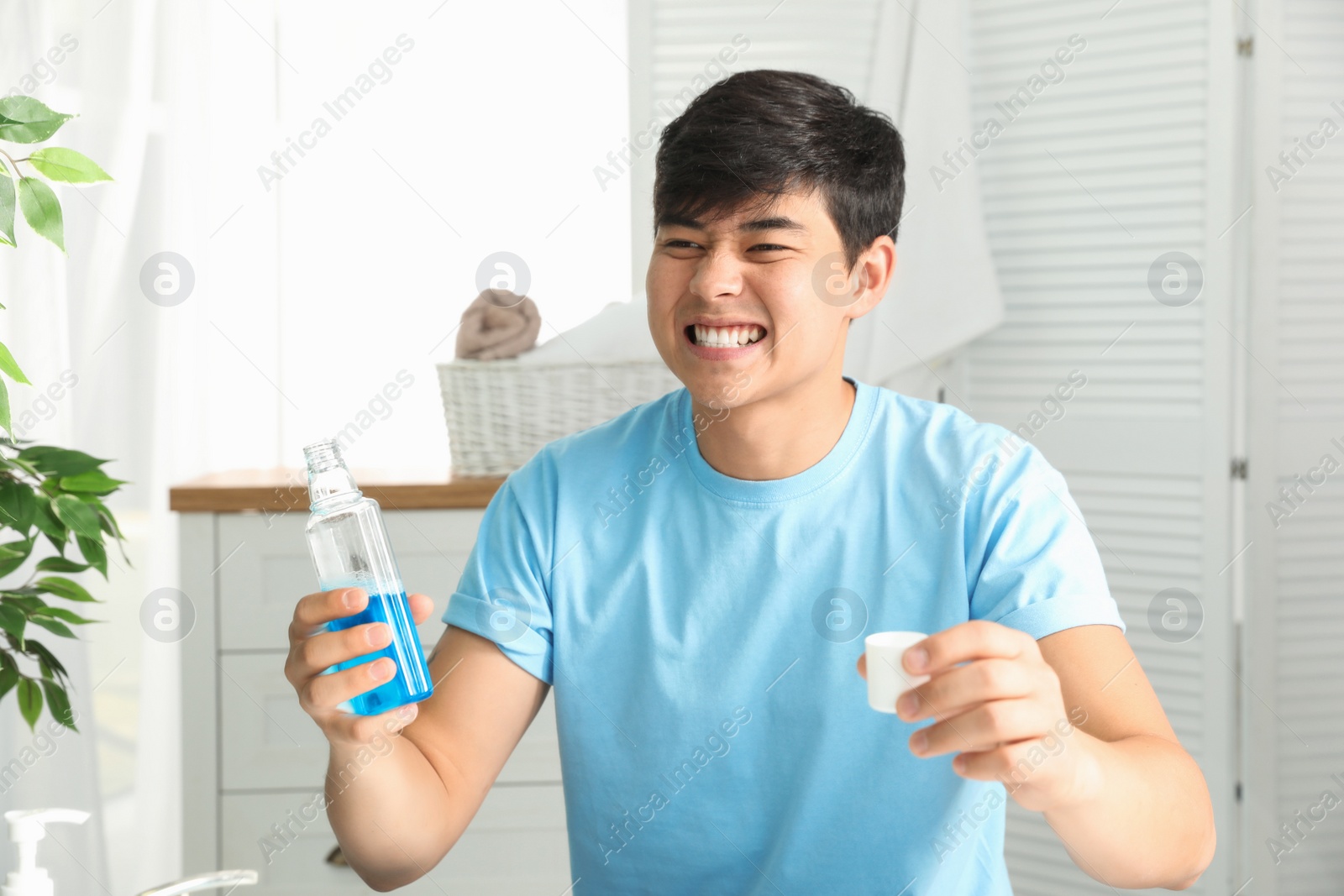 Photo of Man holding bottle and cap with mouthwash in bathroom. Teeth care