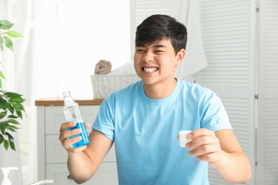 Man holding bottle and cap with mouthwash in bathroom. Teeth care