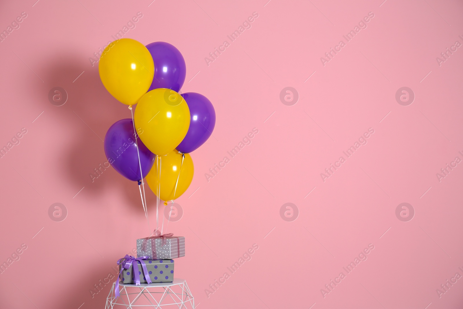 Photo of Bunch of bright balloons and gifts on table against color wall. Space for text