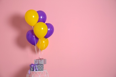 Bunch of bright balloons and gifts on table against color wall. Space for text