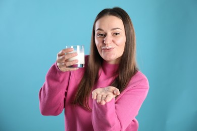 Photo of Happy woman with milk mustache holding glass of drink on light blue background