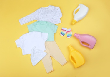 Photo of Flat lay composition with detergents and children's clothes on yellow background