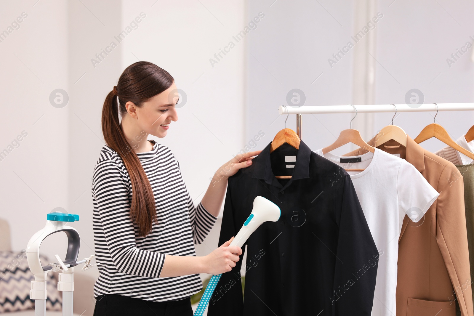 Photo of Woman steaming black shirt on hanger at home